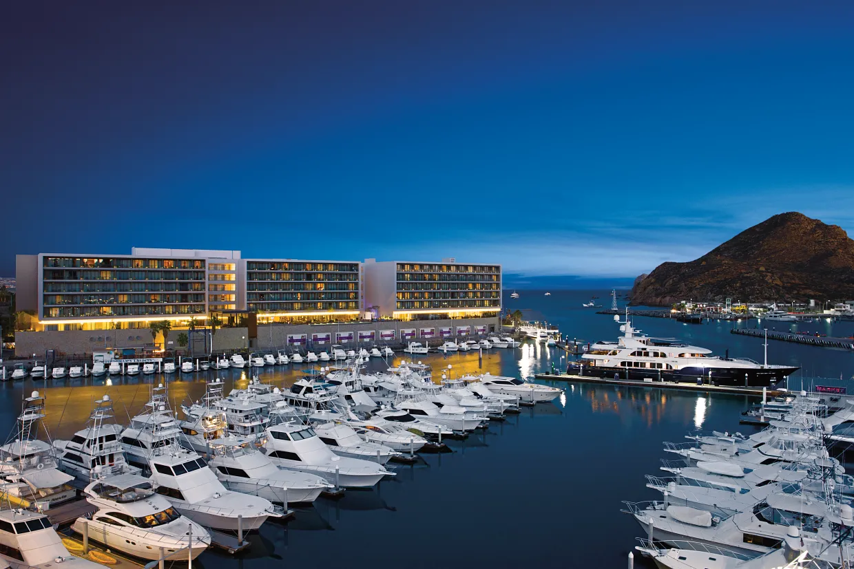 Aerial night view of Breathless Cabo San Lucas overlooking the marina with yachts and dramatic twilight sky.