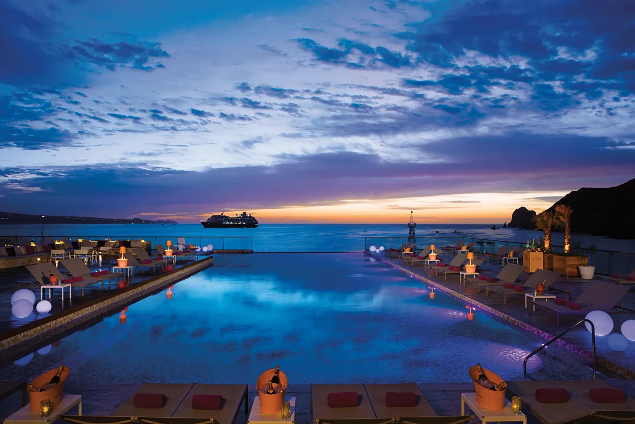 Nighttime rooftop pool area at Breathless Cabo San Lucas with ocean views and glowing lights.