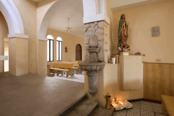 Interior of the Church of Saint Luke in Cabo San Lucas with arches, wooden benches, and religious statues.